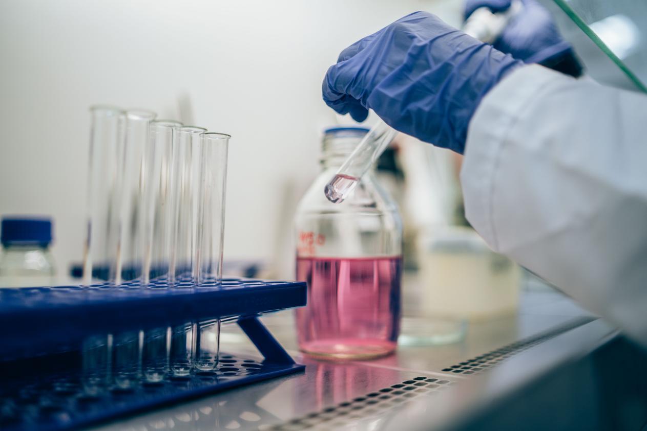 A clear glass bottle holding a pink liquid sample